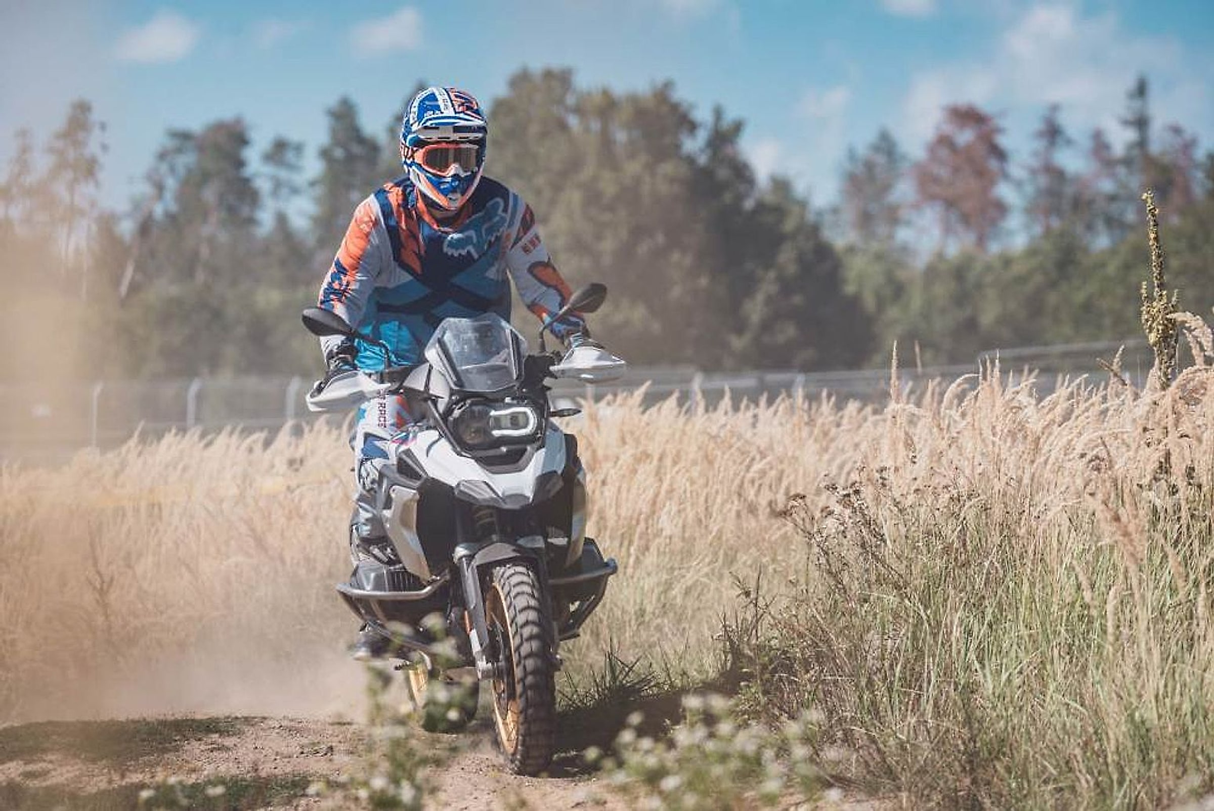 Motorkář v enduro dresu jede po prašné cestě lemované vysokou trávou