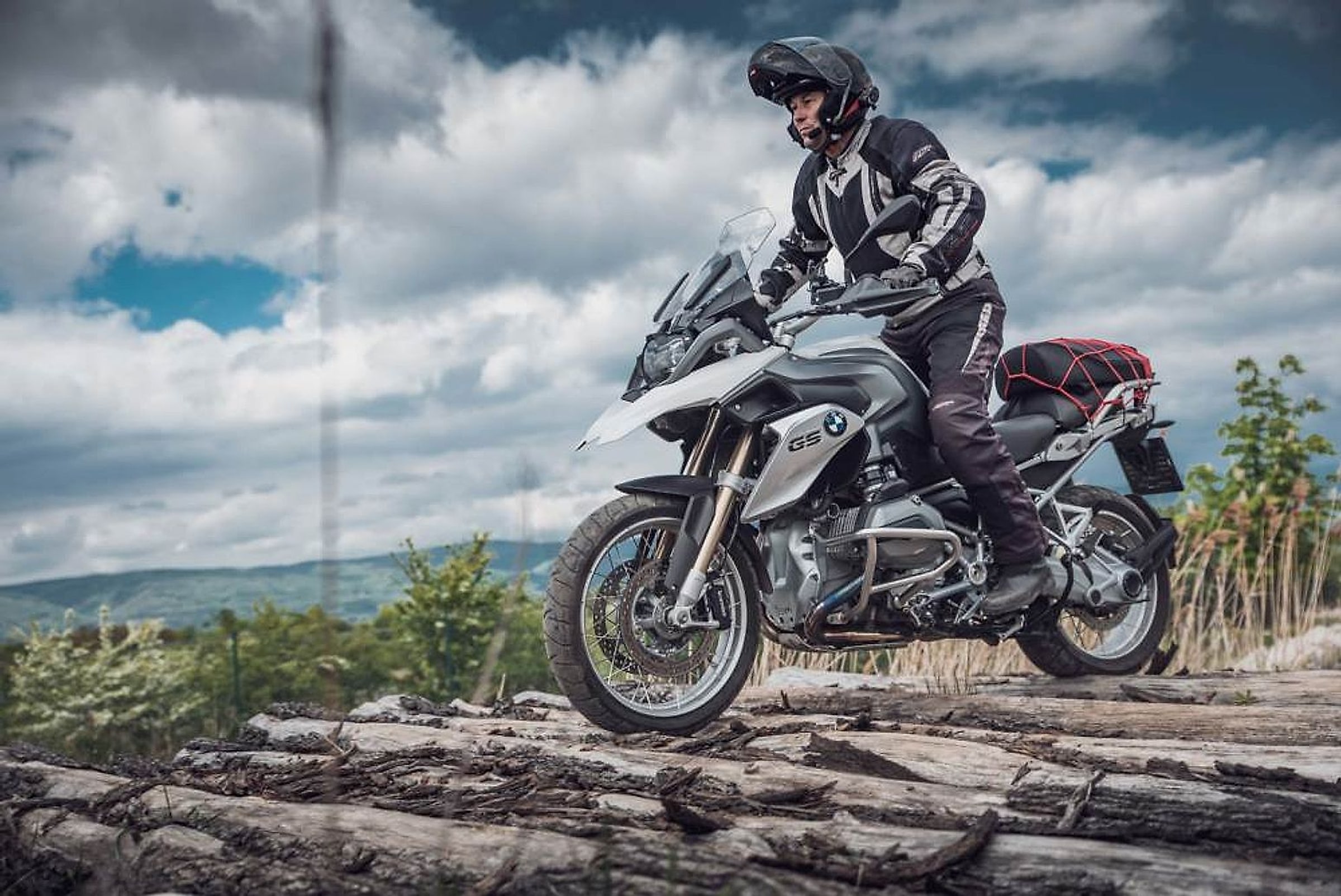 Motorkář na BMW R 1200 GS přejíždí naskládané klády v terénu