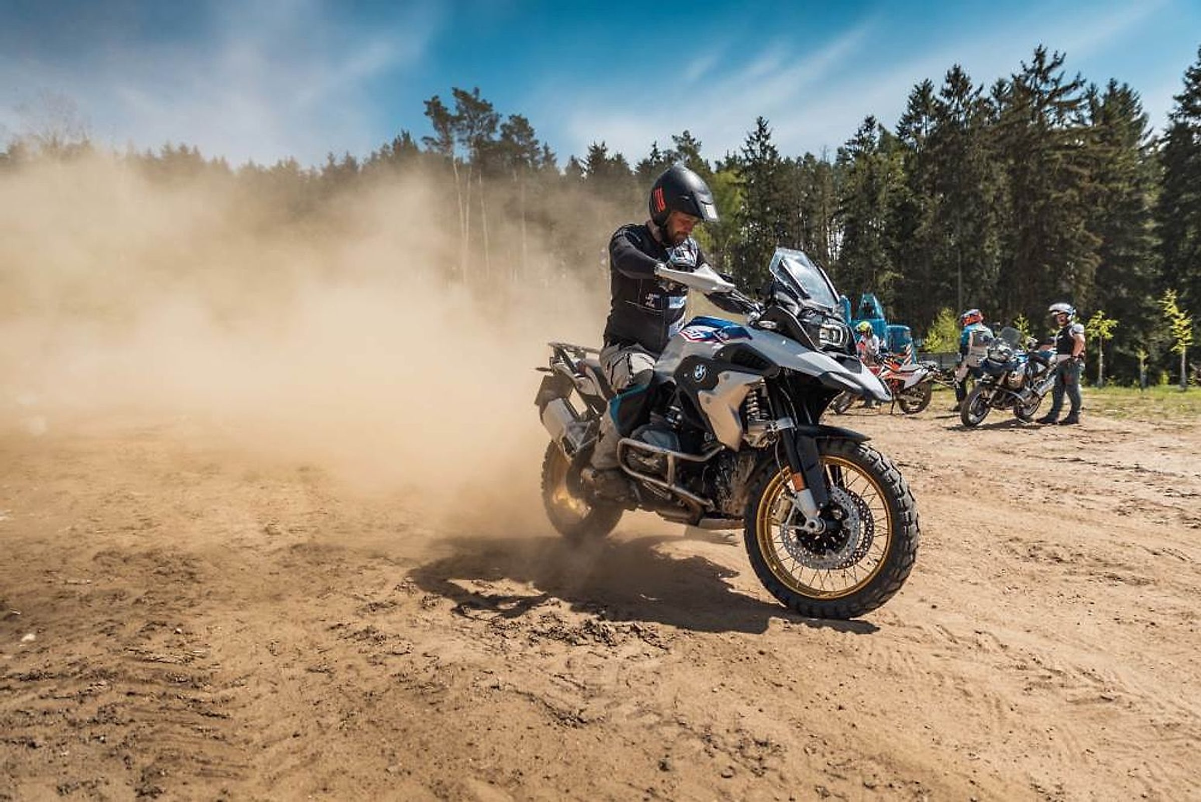 Jezdec na BMW GS zvedá oblak prachu na písčité výcvikové ploše