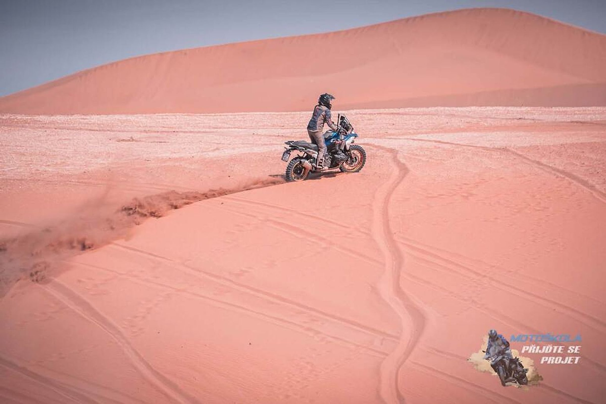 Motorkář na BMW GS jede po hřebeni písečné duny v Maroku